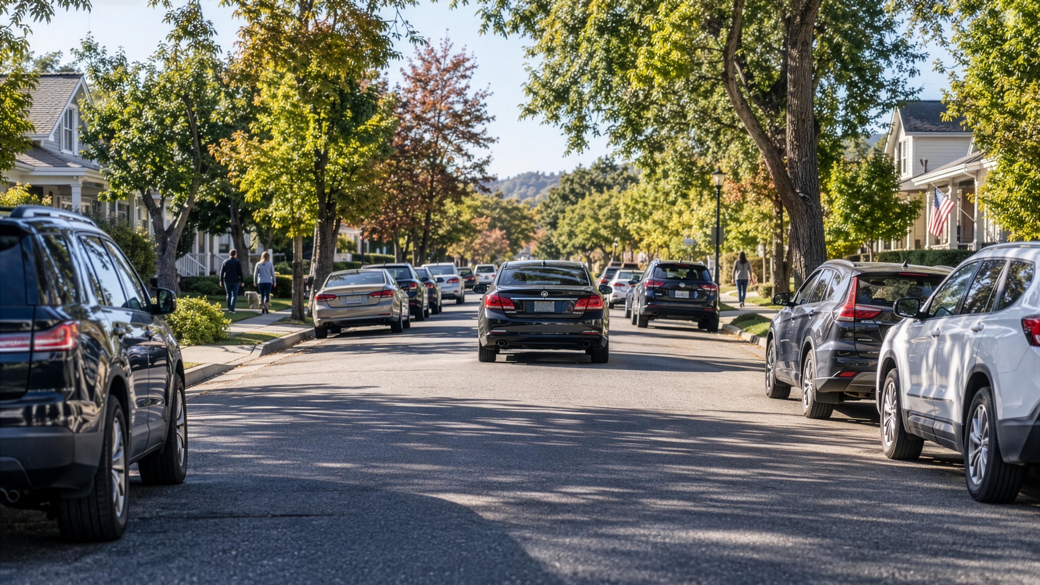 Passenger vehicle driving through a residential neighborhood with parked cars, sidewalks, driveways, and pedestrians nearby